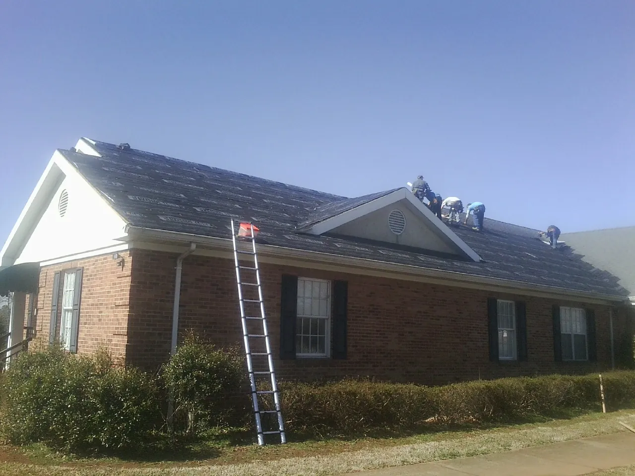Crew tearing shingles off a brick ranch roof with a ladder set — Emergency Roof Repair work by our crew in Pawcatuck