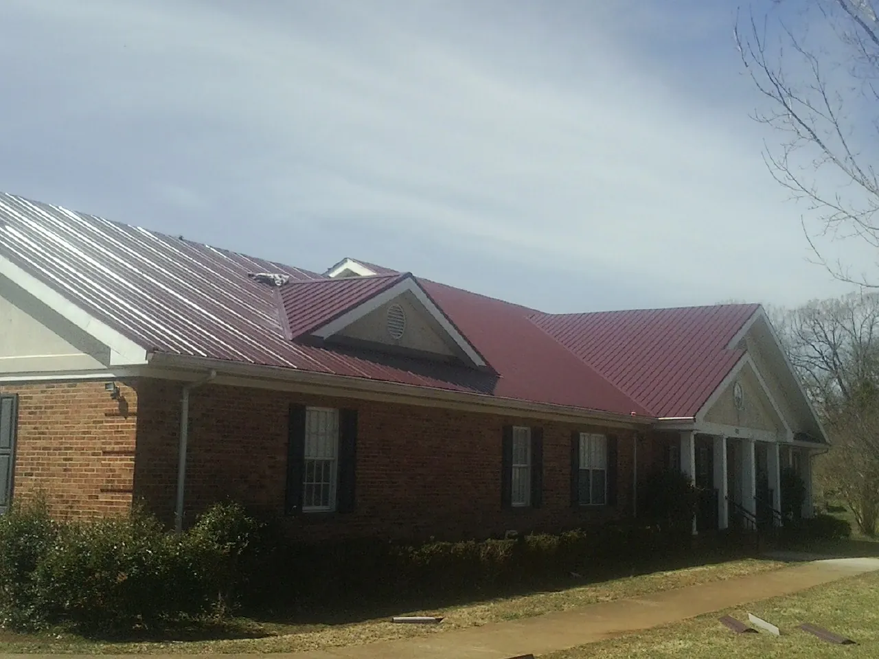 Red metal roof with gabled entries on a long brick building, from a Hail Damage Roof Repair job in Pawcatuck