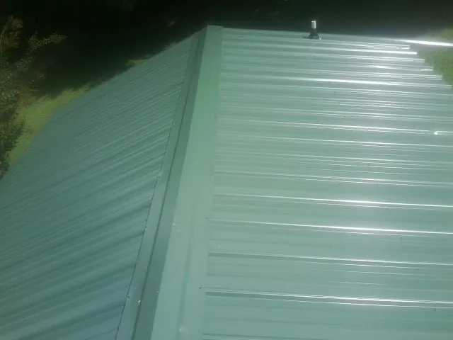 New green metal panels meeting at the ridge of a roof — Flat Roof Repair work by our crew in Pawcatuck