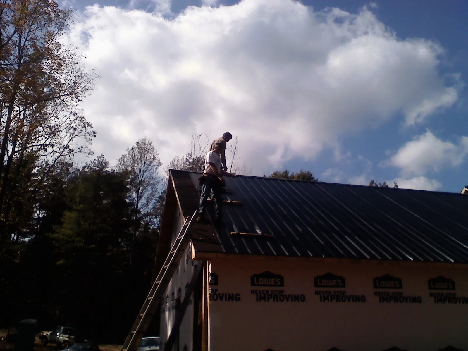 Roofer fastening dark metal panels high against a cloudy sky, from a Roof Inspection job in Pawcatuck