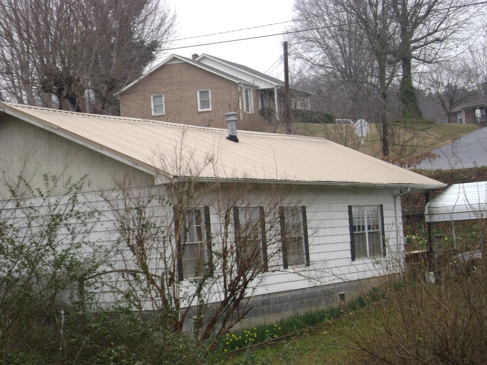 Tan metal roof on a white sided house set into a hillside — Commercial Roofing by Roofing Brothers in Pawcatuck