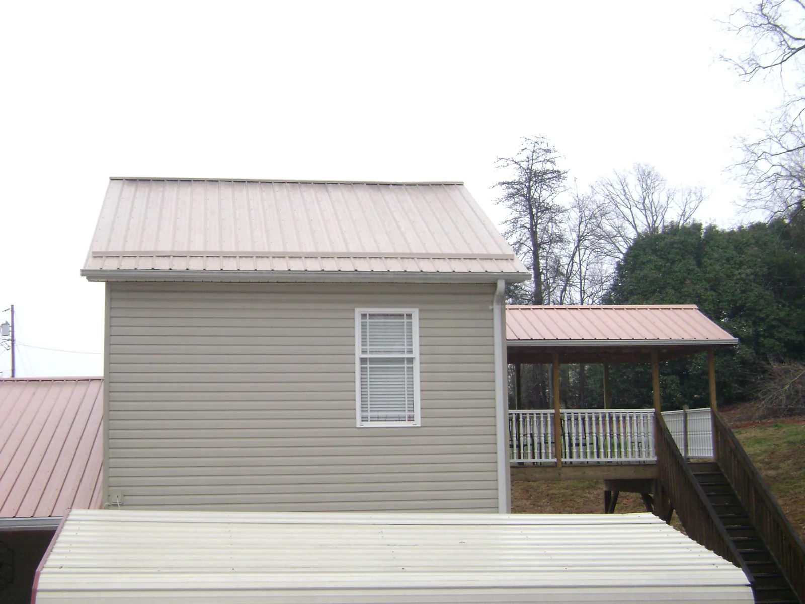 Tan metal roofs on a two story addition and attached porch, from a Roof Replacement job in Pawcatuck