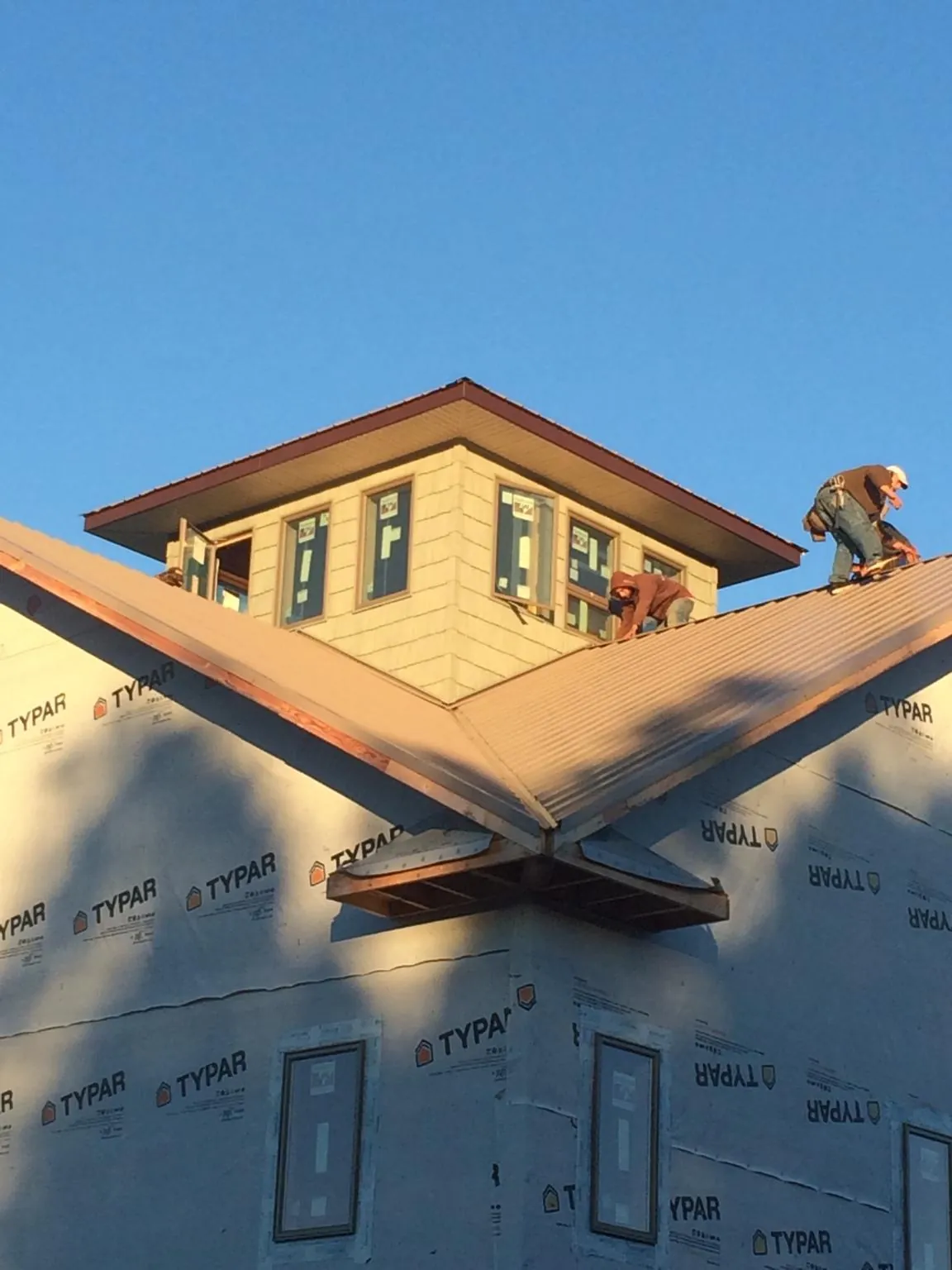 Roofers working around a rooftop cupola on a new metal roof at sunset — Roof Waterproofing in Pawcatuck by Roofing Brothers